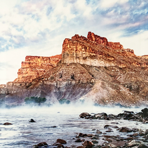 Photo print on metal of the perspective at a rocky shore line looking at the Green River in Utah, witha large rocky mountionous structure in the background against a pink and blue cloudy streaked sky with mist rising from the waters.